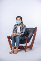 An uncomfortable woman sitting on a chair and wearing a mask photo