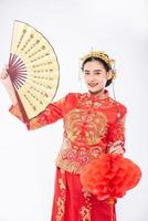 Mujer vistiendo traje cheongsam sostenga el abanico chino y la lámpara roja para mostrar en el gran evento del año nuevo chino