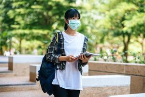 Female students wear masks, stand on stairs and hold books. photo