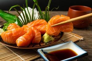 sashimi, salmón, palillos de comida japonesa y wasabi en la mesa de madera