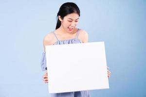 Imagen de una chica asiática sosteniendo una pizarra blanca, aislado sobre fondo azul. foto