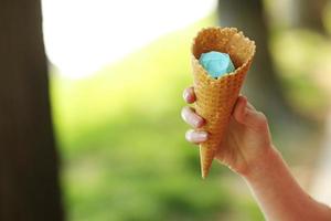 mano femenina que sostiene el cono de oblea con helado azul. de cerca, producto de alta resolución. helado azul en la mano.