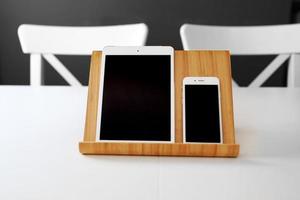 a white tablet and a smartphone with a black screen on a stand on a white table. office workplace photo