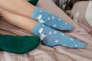 Legs with cute blue socks with white bears and green socks on the bed. Colored socks photo