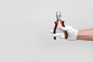 Man's hand in white glove raised holding a black and red tool pliers, wire cutter. Isolated on white background. Open, clean, ready to cut form. Mock up copy space. photo