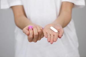 Close up view of young woman making choice between menstrual cup and tampon, on white background. Gynecology concept photo