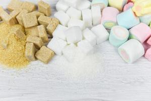 azúcar morena, azúcar blanco, terrones de azúcar y dulces de colores sobre el fondo de la mesa sin azúcar en la dieta causa obesidad diabetes y otros problemas de salud foto
