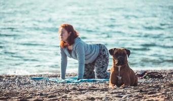 Mujer joven haciendo yoga y estiramientos en la playa con su perro foto