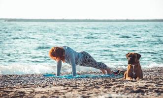 girl doing yoga and stretching on the beach with her dog photo