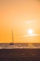 Little white boat floating on the water towards the horizon in the rays of the setting sun photo