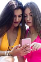 two girls in swimsuits using their cell phones at the pool photo