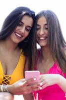 two teenage girls in a swimsuit sitting on the lawn of the pool watching the mobile photo