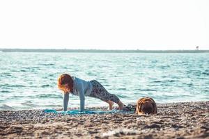young woman doing yoga and stretching on the beach with her dog