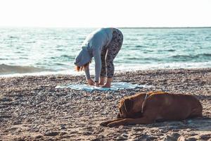 girl doing yoga and stretching on the beach with her dog photo