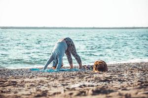young woman doing yoga and stretching on the beach with her dog photo