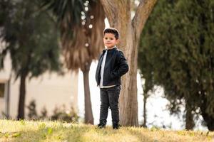 Fashion little boy wearing a leather jacket. Park or forest, outdoor photo