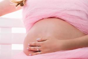 Mujer embarazada sentada tocando su vientre con ropa rosa foto