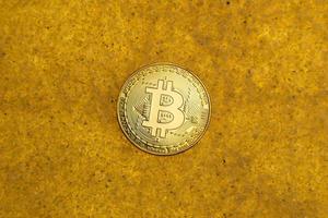 one bitcoin crypto coin on a shiny golden sand background with backlight, top view. photo