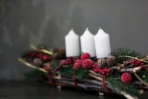 Velas blancas de Navidad en un montón de ramitas decoradas con conos de abeto y bayas sobre un fondo gris foto