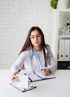 Young doctor woman writing in her cabinet filling medical history or anamnesis photo