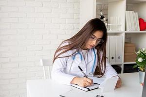 Young doctor woman writing in her cabinet filling medical history or anamnesis photo
