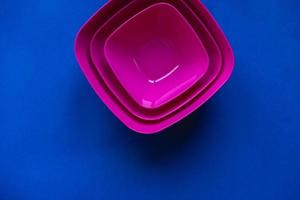 Set of pink plates on blue background. Plastic utensils for the kitchen photo