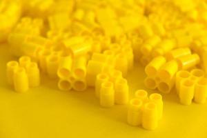 Yellow plastic building blocks on yellow background. Background of plastic details building blocks. Parts of bright small spare parts for toys photo