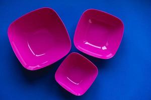 Set of pink plates on blue background. Plastic utensils for the kitchen photo