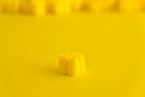 Yellow plastic building block on yellow background photo