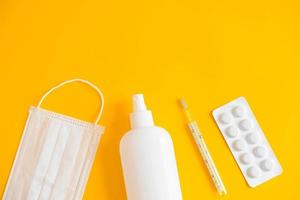 A set of medical disposable mask, antiseptic, pills and a mercury thermometer on a yellow background. Medical hygiene and virus protection concept