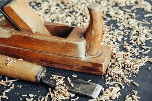 Old hand plane and chisel with wooden shavings on black background. Old woodworking hand tool. Copy, empty space for text photo