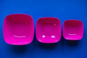 Set of pink plates on blue background. Plastic utensils for the kitchen photo