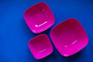 Set of pink plates on blue background. Plastic utensils for the kitchen photo