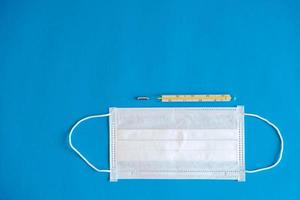 Medical disposable mask and a mercury thermometer on a blue background. Protection concept
