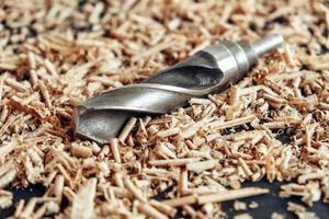 Wood drill bit with wooden shavings on black background photo
