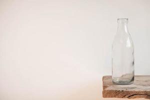 Glass transparent bottle on wooden table on white wall background photo