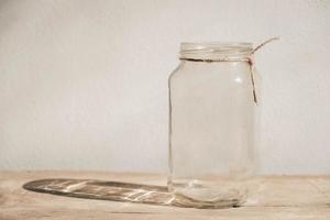 Frasco de vidrio transparente sobre la mesa de madera sobre fondo de pared blanca foto