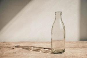 Glass transparent bottle on wooden table on white wall background photo