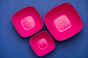 Set of pink plates on blue background. Plastic utensils for the kitchen photo