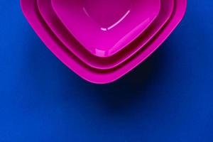 Set of pink plates on blue background. Plastic utensils for the kitchen photo