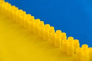 Yellow plastic building blocks on blue and yellow background. Pieces and elements of constructor. Parts of bright small spare parts for toys. Top view. Copy, empty space for text photo