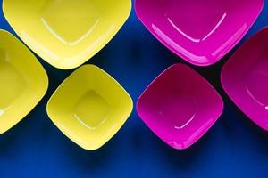 Set of pink and yellow plates on blue background. Plastic utensils for the kitchen photo