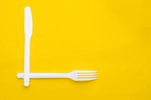 Plastic white fork and knife on yellow background. Cooking utensil photo