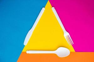 Plastic white fork, knife and spoon on multicolored background photo