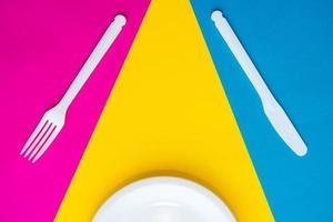 Plastic white fork, knife and plate on multicolored background photo