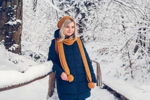 Beautiful young woman in a winter forest. Winter portrait of woman dressed in cap and scarf