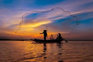 Pescador asiático con su bote de madera en el río de la naturaleza temprano en la mañana antes del amanecer