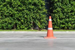 Single orange traffic cone on concrete street road with small park in background photo