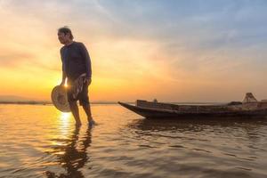 Pescador asiático con su bote de madera yendo a pescar peces de agua dulce en el río natural temprano durante el tiempo del amanecer