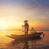 Silueta pescador asiático sosteniendo una red para pescar peces de agua dulce en el lago natural durante el amanecer